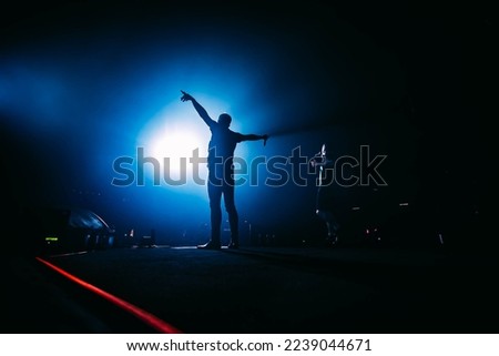 Popular singer on stage in front of crowd on scene in night club. Bright stage lighting. Silhouette of a dancing person.