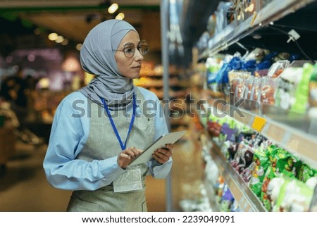 woman Seller in super market in hijab with tablet checking products using pocket computer, Muslim woman near shelves with products and goods. Royalty-Free Stock Photo #2239049091