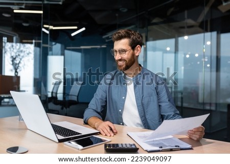 Mature businessman in shirt doing paperwork, man working with documents, contracts and bills sitting at table using laptop at work, financier accountant with beard and glasses. Royalty-Free Stock Photo #2239049097