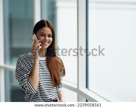 Woman smile talking on the phone video call online communication, woman at the window in the office in the city