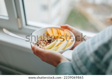 Top view for breakfast in the hands of an unrecognizable woman a spoon in a plate with granola and raw bright fruits. Weight loss breakfast. Cellulose and coarse fibers. Vitamins and minerals. Royalty-Free Stock Photo #2239069865