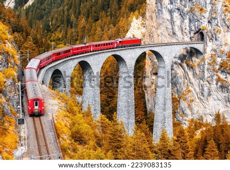 Bernina express glacier train on Landwasser Viaduct in autumn, Switzerland. Scenic view of railroad bridge in orange mountain forest in Swiss Alps. Theme of railway, nature, fall season and travel. Royalty-Free Stock Photo #2239083135