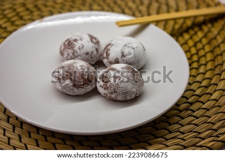 Wooden chopsticks and traditional Japanese dessert mochi or daifuku in rice dough. Four mochi ice cream balls on white round plate on brown rattan doily. Asian sweet delicious food dessert top view.