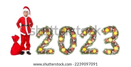 Boy Santa Claus holding a christmas sack and 2023 number made by christmas tree branches isolated on white background