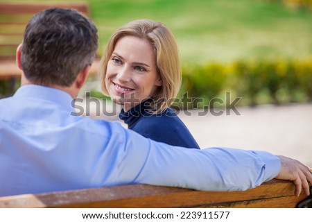 Adult smiling couple looking on each other sitting on bench. beautiful elegant mid age couple daydreaming outdoors