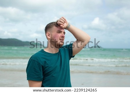 Guy is suffering from heat, man with heatstroke. Having sunstroke at summer hot weather. Dangerous sun, boy under sunshine. Headache, feeling bad. Person holds hand on head at sea, beach Royalty-Free Stock Photo #2239124265