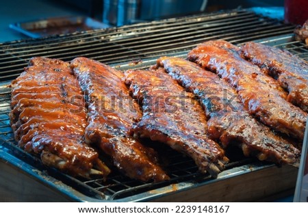 Delicious pork ribs grilled on the BBQ grill in the kitchen with smoke and flames, ready to serve.