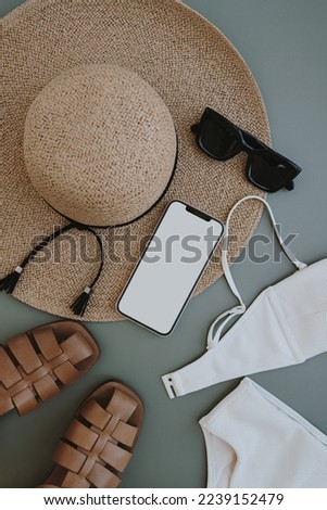 Flatlay of aesthetic women's fashion accessories. Mobile phone with blank copy space screen. Stylish female straw hat, swimsuit, sunglasses, sandals on pastel background. Top view, flat lay