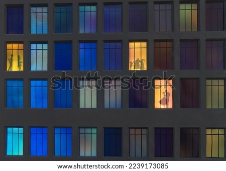 the wall of a night house in the illuminated windows of which silhouettes of people are visible.
