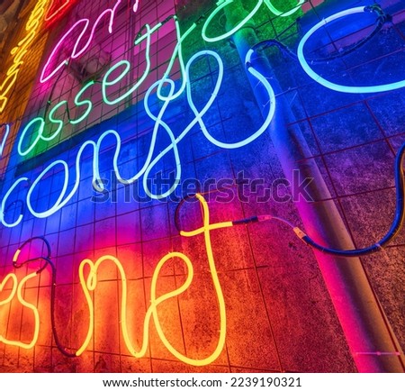 Illuminated letters and words made with neon lights and LEDs of many colors with words in the Catalan language with evocative concepts of hope and wishes on a wall. Low angle view.