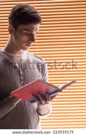 young male student reading book. closeup of man standing near window with jalousie
