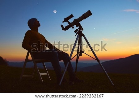 Man with astronomy telescope looking at the night sky, stars, planets, Moon and shooting stars. Royalty-Free Stock Photo #2239232167