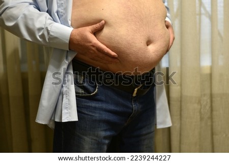 In the picture, a shirtless man with a large fat belly holds his hands on his belt.