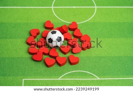 Football ball and red hearts on green grass background