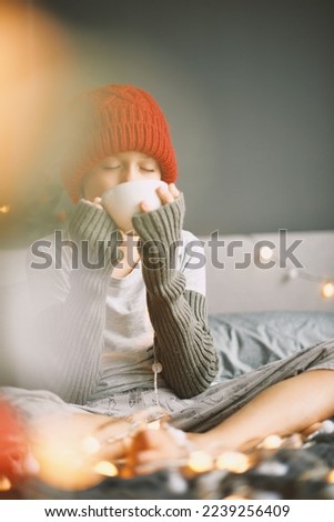 Happy boy in red knitted winter hat holding, drinking cup hot beverage chocolate cocoa with marshmallows at home Merry Christmas and Happy New Year Winter holidays spirit Cozy candid moment