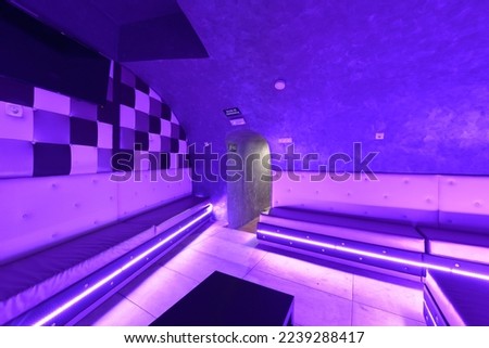 Subway nightclub room with white upholstered armchairs along the wall and led lights on the skirting boards