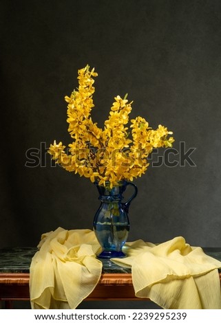 Yellow spring flowers in a blue transparent vase on a gray background. Next to it is a yellow scarf. Still life. Painting. Card. Health. Calm. The beauty. Wishes.