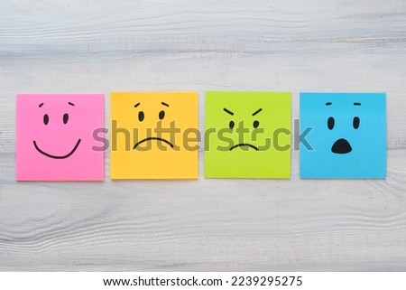 Basic emotions are joy, sadness, anger, fear or surprise. Four colorful squares with emotions on a wooden background