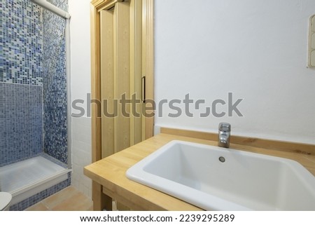 White porcelain sink on a beech wood cabinet and shower cabin with blue tile