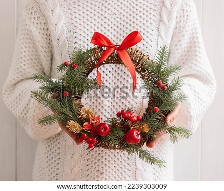 Woman holds in her hands festive Christmas wreath of fir branches with red berries bright ribbons