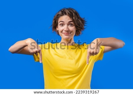 Pretty woman pointing down to advertising area. Blue background. Young lady asking to click to subscribe below. Copy space for your commercial idea, promotional content. High quality photo Royalty-Free Stock Photo #2239319267