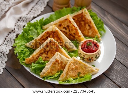 Mini Flatbread Wraps with cheese and ham filling. Fried patties from thin Armenian lavash served with tomato sauce on a white plate with lettuce leaves. Selective focus, horizontal, wooden table. Royalty-Free Stock Photo #2239345543