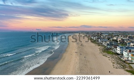 aerial shot of the coastline with blue ocean water and homes along the sand on the beach, cars driving on the street and blue sky with clouds in Huntington Beach California USA

