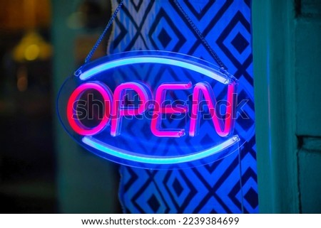 Neon sign with blue and red color that says open in the window of a shop or restaurant in the downtown city of the neighborhood. Late in the day in the city streets downtown in place of business.