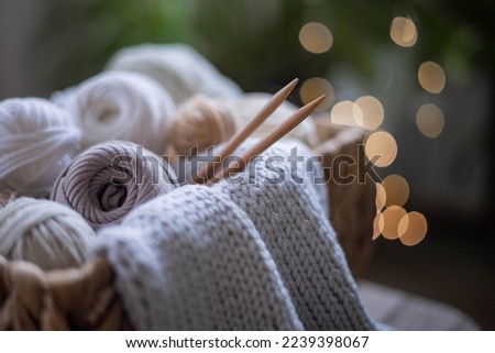 Cozy homely atmosphere. Female hobby knitting. Yarn in neutral shades in a basket woven from natural jute. The beginning of the process of knitting a women's sweater.