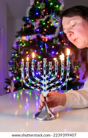 Jewish woman blows out the candles on the Hanukkah menorah with nine candles.