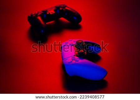 White and black gamepads illuminated red light on a dark background, game controller for video games.