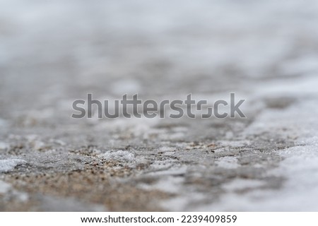 macro ground level closeup view of rock salt ice-melt on concrete with a frozen layer. 