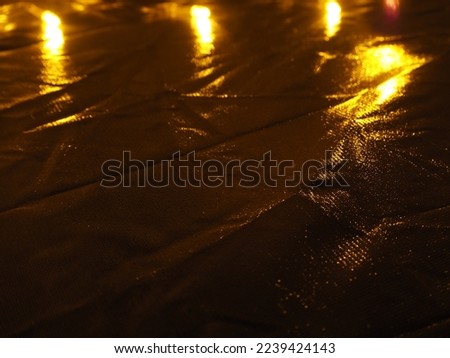 Golden reflections on plastic sheet in darkness for background