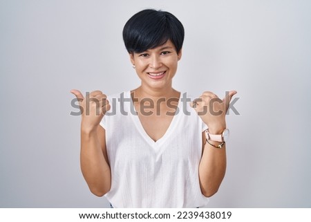 Young asian woman with short hair standing over isolated background success sign doing positive gesture with hand, thumbs up smiling and happy. cheerful expression and winner gesture. 