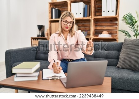 Young hispanic woman working online at consultation office with open hand doing stop sign with serious and confident expression, defense gesture 