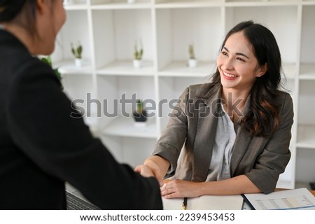 Successful and professional millennial Asian businesswoman smiling, shaking hand with her business partner in the business cooperation meeting. Royalty-Free Stock Photo #2239453453