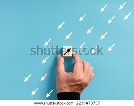 Unique, think different, individuality. Swim against the stream and standing out from the crowd. Male hand placing a wooden block with an opposite pointing arrow against the flowing arrows.