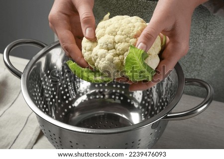 Woman holding fresh cauliflower cabbage above colander at wooden table, closeup