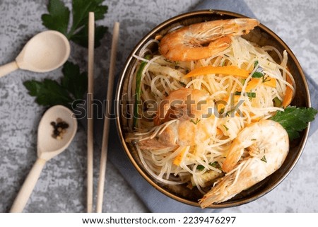Funchosa salad with shrimps in a bowl with chopsticks and parsley leaves on a gray background. Top view