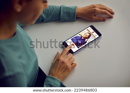 Woman looking for a boyfriend, using a modern online dating app on her mobile phone, looking at profile pics of different men and giving likes to those she likes. Cropped shot, close up