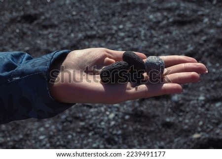 Close up woman showing black pebbles on palm concept photo. Front view photography with black sand beach on background. High quality picture for wallpaper, travel blog, magazine, article