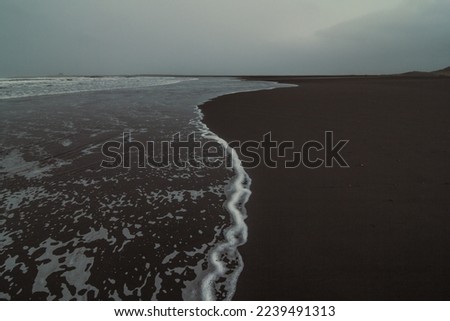 Wave rolling on black sand landscape photo. Beautiful nature scenery photography with cloudy sky on background. Idyllic scene. High quality picture for wallpaper, travel blog, magazine, article