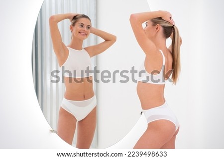 Slim young woman standing and posing in front of the mirror in white bikini