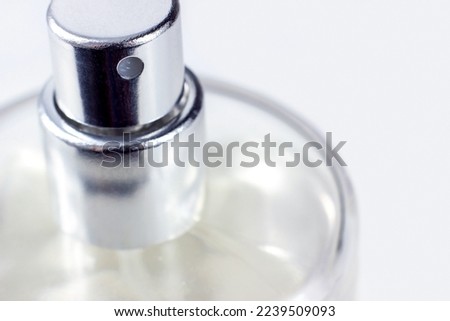 Silver perfume spray cap and transparent glass bottle on light background close up with copy space