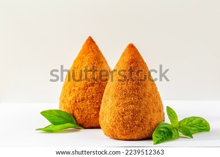  Italian rice balls that are stuffed, coated with breadcrumbs and deep fried.  Filled with ragu, mince meat, caciocavallo cheese and green peas. Conical-shaped arancini with basil on white background Royalty-Free Stock Photo #2239512363