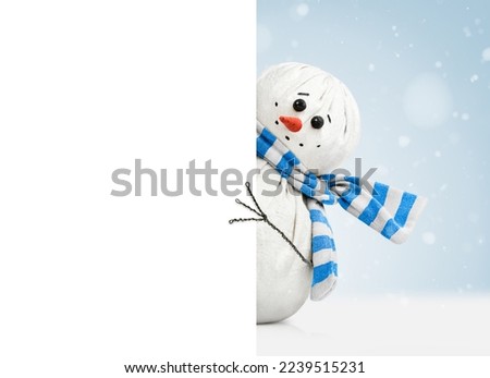 cute snowman in a striped scarf peeks out from behind a white banner with copy space