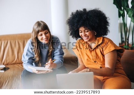 Two happy young businesswomen having a video call in an office lobby. Cheerful young businesswomen attending an online meeting. Female entrepreneurs working together in a modern workplace. Royalty-Free Stock Photo #2239517893