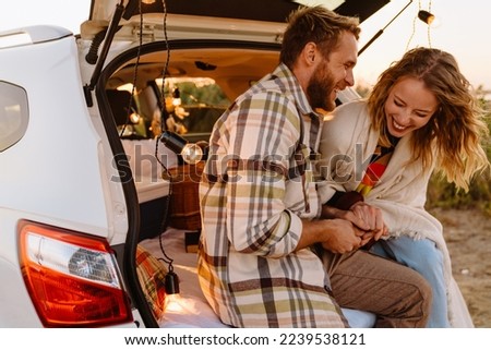 Happy young white couple smiling and sitting in car trunk together outdoors Royalty-Free Stock Photo #2239538121
