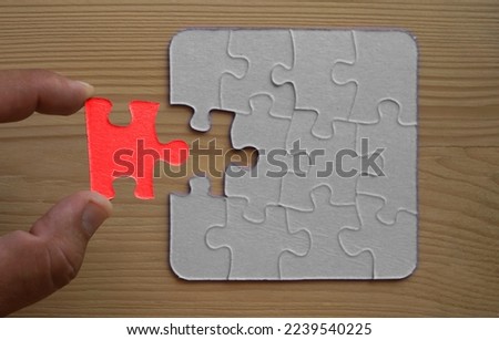male Hand and red puzzle on background without one piece. Wooden table background. Finding the Missing Piece. 
