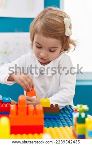 Adorable caucasian girl playing with construction blocks standing at kindergarten